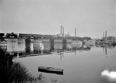 166643 Gezicht op de tijdelijk herstelde spoorbrug over de Maas te Maastricht, tijdens het passeren van een gemengde trein.